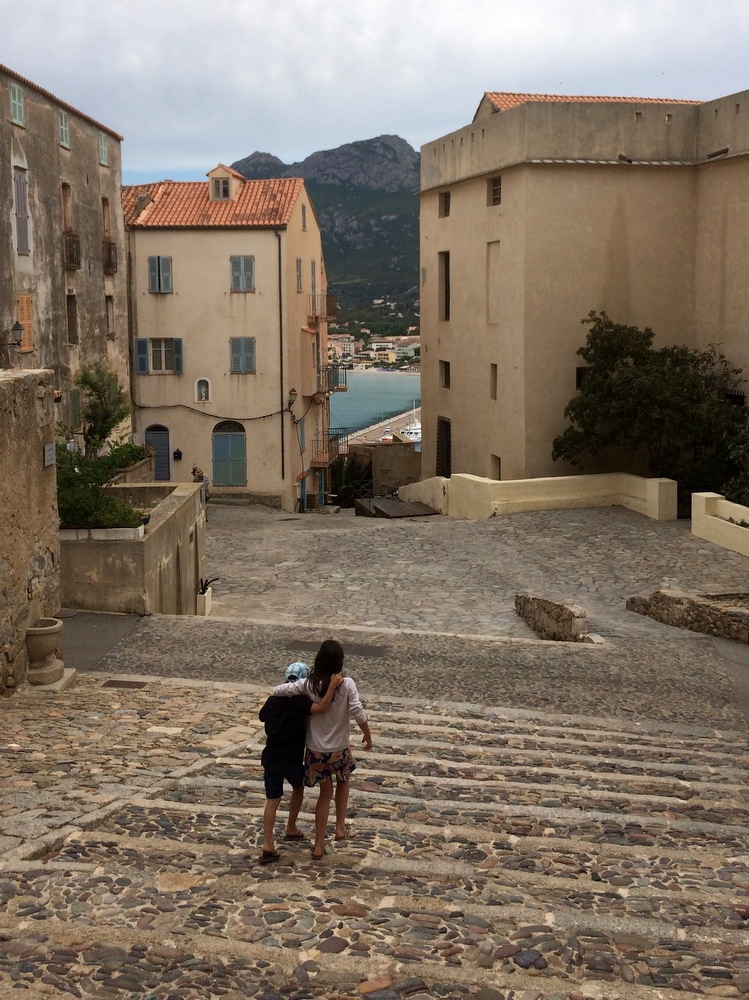 Brother and sister at Calvi's citadell walking down stairs arm in arm.