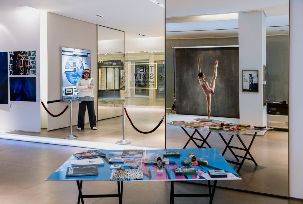 A portrait of photo artist Wolfgang W. Sohn in 'The Sixty' gallery, Düsseldorf, featuring reflections of a ballet dancer in the background. [Copyright Jan Söhlke]